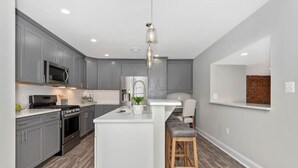 A modern kitchen with grey cabinets, a white island, and a wooden stool.