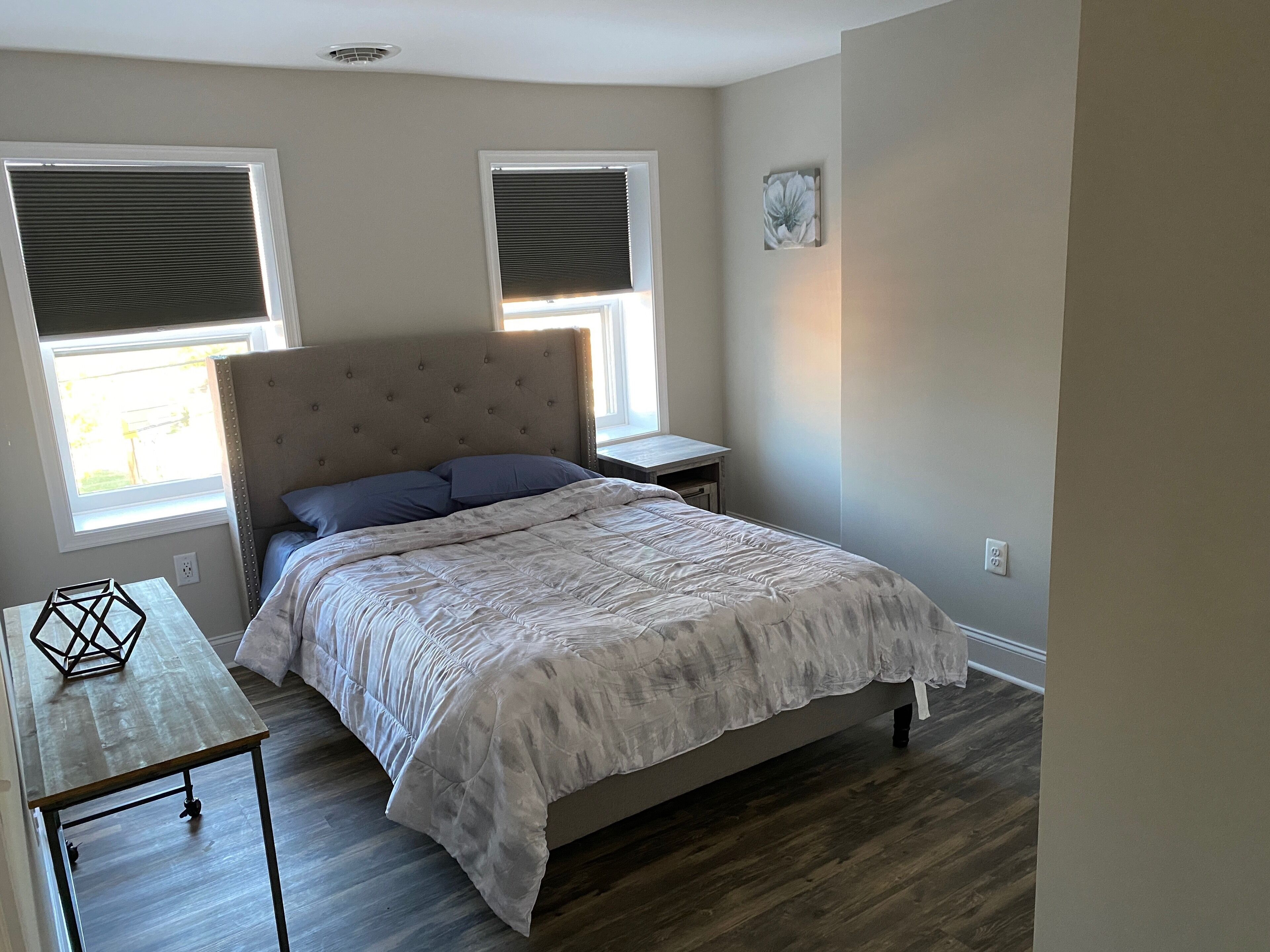 Une chambre à coucher avec un lit, deux fenêtres, une table de chevet et une petite table.