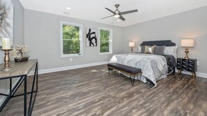 A bedroom with a bed, a bench, a desk, and two windows.