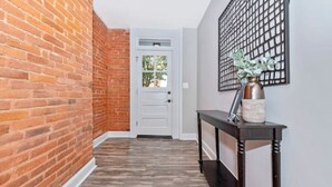 A hallway with brick walls, a white door, and a black console table with a vase.