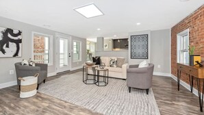 A spacious living room with a grey sofa, a coffee table, and a patterned rug.