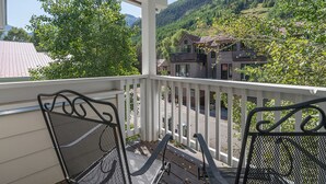 Een balkon met twee metalen stoelen, uitkijkend op een straat en een huis met balkon.