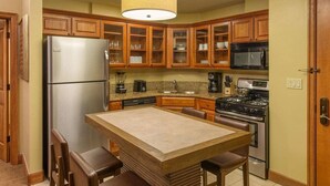 Una cocina con armarios de madera, un refrigerador de acero inoxidable, un microondas, una estufa y una isla central con sillas.