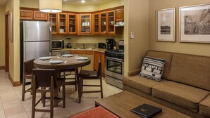 Cocina compacta con armarios de madera, refrigerador, estufa y un comedor con mesa redonda y sillas.