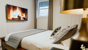 Una camera da letto con un letto, una TV a parete, una finestra con tende e una lampada su un comodino.