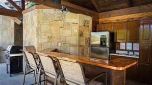 Une cuisine dotée d’un mur de crédence en pierre, d’un réfrigérateur en acier inoxydable et d’un coin bar avec des tabourets.