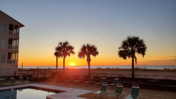 A pool area with lounge chairs and a view of the sunset over the ocean. - Direct Oceanfront 3 bedroom 2.5 baths Pelicans Watch unit on popular Shore Drive (Myrtle Beach)