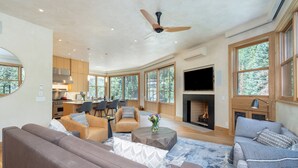 A spacious living room with a fireplace, large windows, and a modern kitchen in the background. - THE Tributary by Exceptional Stays (Telluride)