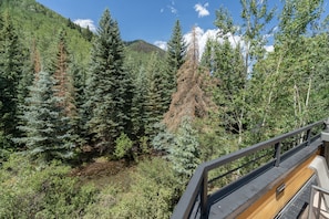A forested mountain area with a wooden deck and metal railing. - THE Tributary by Exceptional Stays (Telluride)