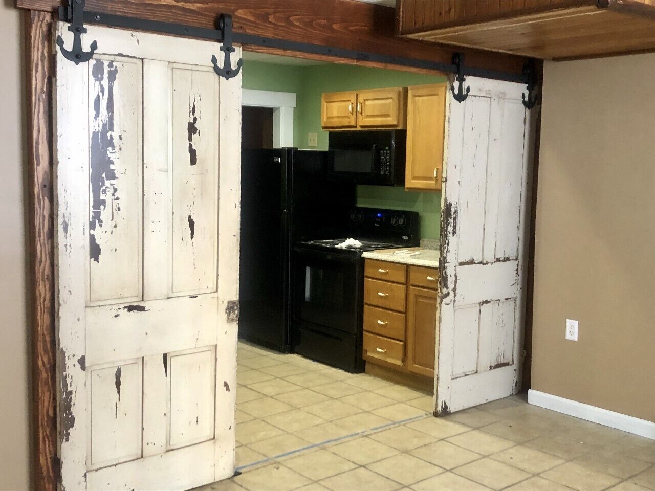 A kitchen with a black refrigerator, microwave, and stove, wooden cabinets, and a white door with peeling paint.