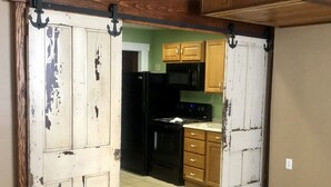 Una cocina con un refrigerador negro, microondas y estufa, armarios de madera y una puerta blanca desconchada.