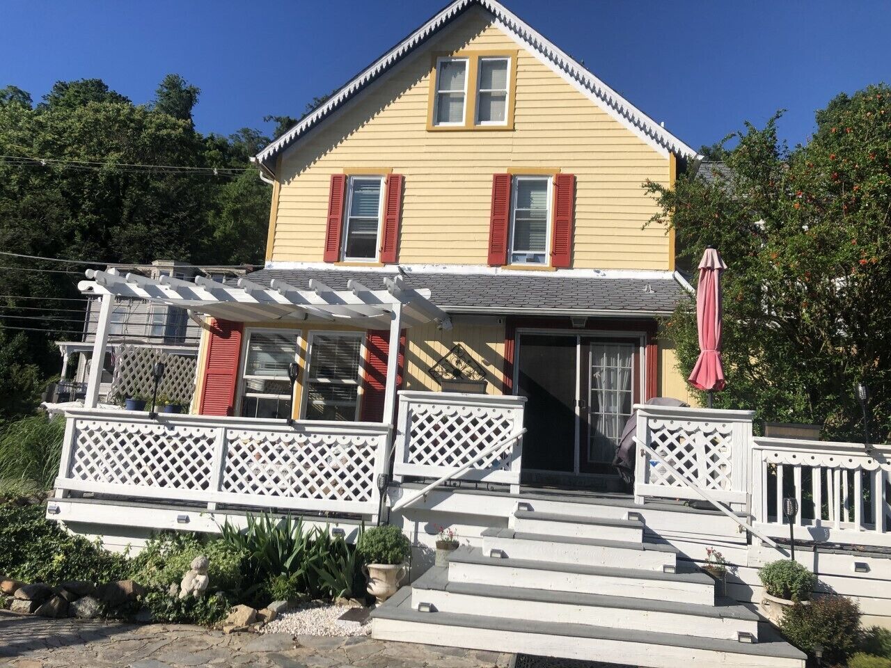 A yellow house with red shutters, a porch with lattice railings, and a red umbrella.