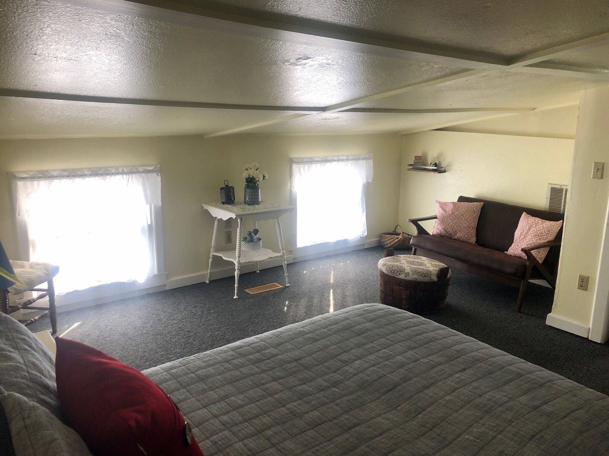 Una habitación amplia con una cama grande, un sofá, una mesita con un florero y una ventana con cortinas.