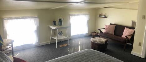 Una habitación amplia con una cama grande, un sofá, una mesita con un florero y una ventana con cortinas.