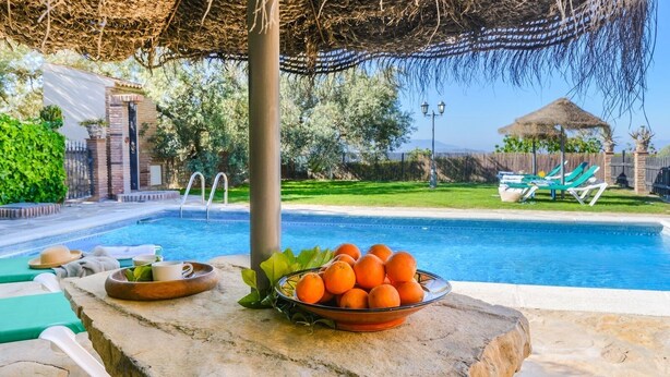 A poolside area with a stone table, a bowl of oranges, and lounge chairs. - Villa Antisa Villanueva de la Concepción by Ruralidays (Málaga)