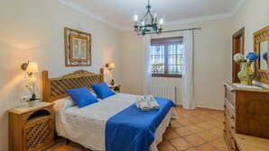 A bedroom with a bed, bedside tables, a chandelier, a window with curtains, and a dresser. - Villa Antisa Villanueva de la Concepción by Ruralidays (Málaga)