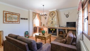 A cozy living room with a fireplace, leather sofas, a wooden coffee table, and a TV mounted on the wall. - Villa Antisa Villanueva de la Concepción by Ruralidays (Málaga)