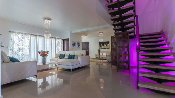 Amplia sala de estar con una escalera moderna y un conjunto de sofás blancos.