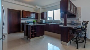 Una cocina amplia con armarios de madera oscura, una isla central y una zona de comedor con sillas de metal.