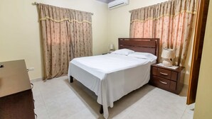 Une chambre avec un lit simple, une table de chevet, une commode et des rideaux.