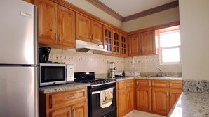 Une cuisine avec des meubles en bois, un réfrigérateur en acier inoxydable, un four à micro-ondes, une cuisinière et une fenêtre.