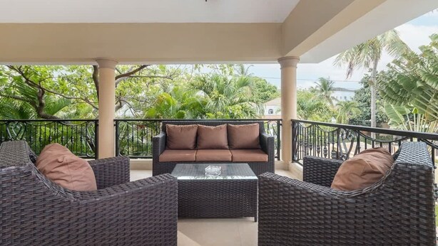 A covered outdoor seating area with wicker furniture and a sofa, surrounded by greenery. - VIP Sosúa Villa | Private Pool & Pool Table (Sosúa)