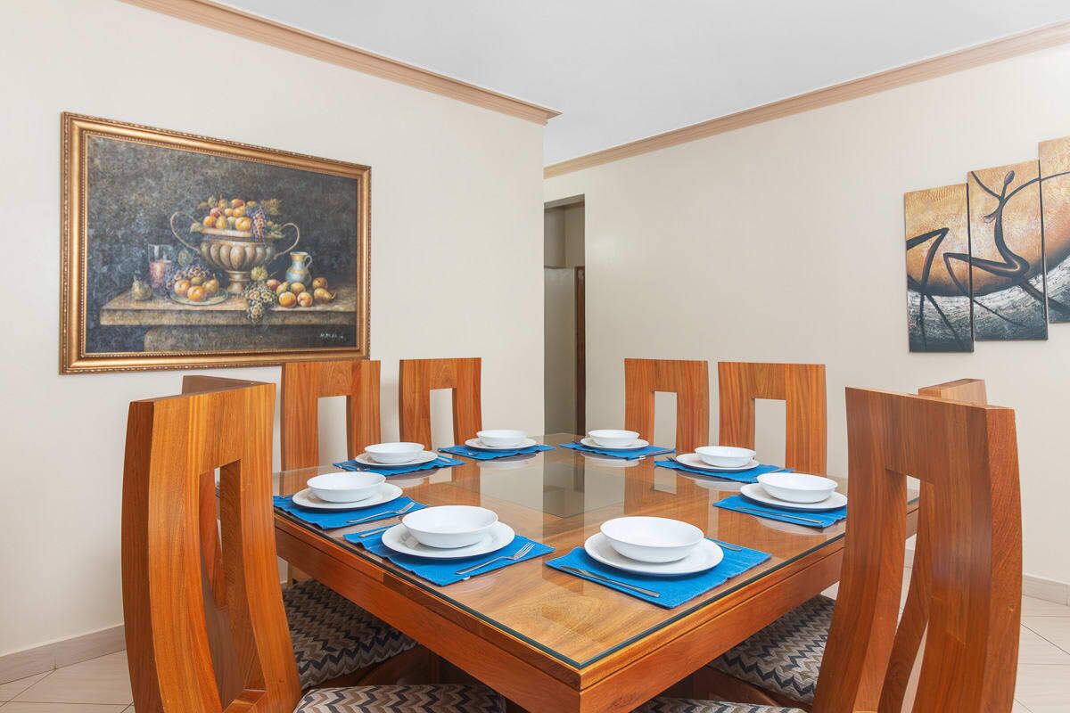 Un comedor con una mesa de vidrio, sillas de madera y manteles individuales azules.