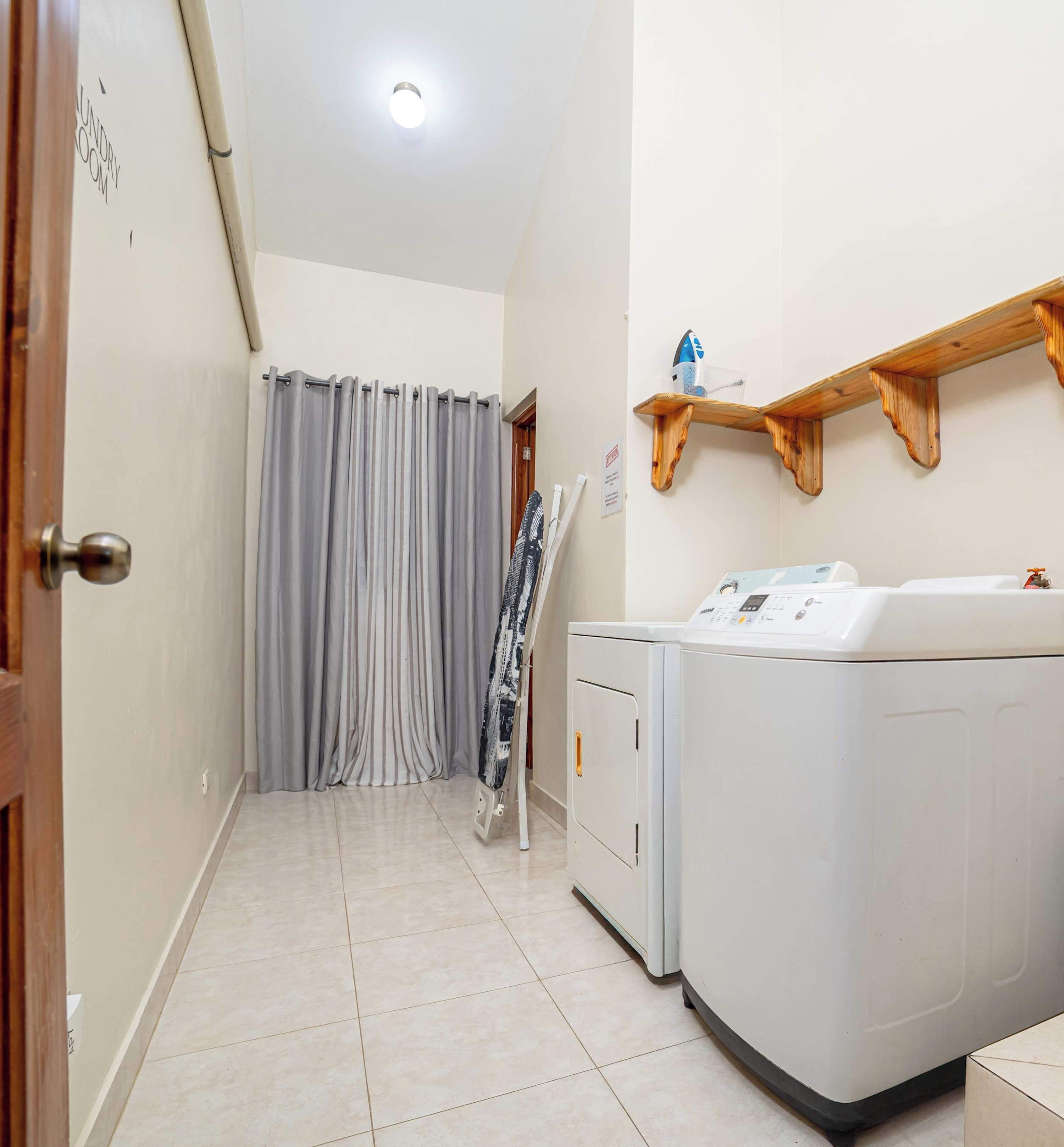 A laundry room with a washing machine, a drying rack, and a wooden shelf with a cup and a container.