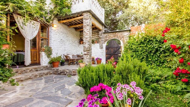 Une cour pavée de pierres, avec un mur en pierre rustique, une porte en bois et un petit espace extérieur aménagé avec des chaises et des tables.