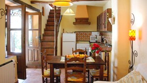 Une cuisine chaleureuse, meublée de meubles en bois, avec une table à manger dressée et ornée de fruits, et un escalier menant à un autre niveau.