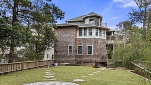 A two-story house with a stone patio, wooden deck, and a fenced backyard.