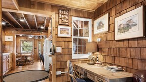 A wooden interior with a dining area, a desk with a lamp, and framed artwork on the walls.