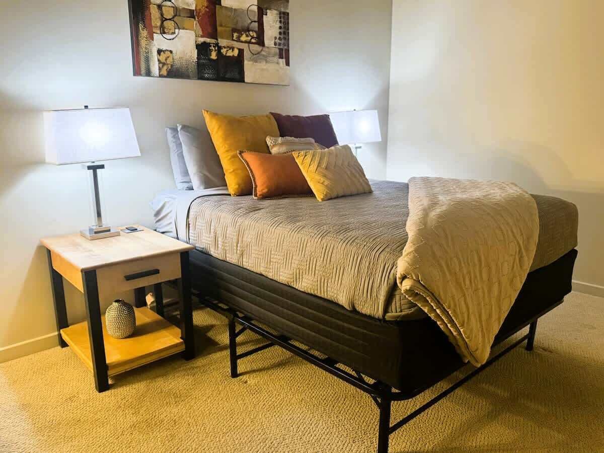 Une chambre à coucher comprenant un lit, deux tables de chevet, une lampe et une œuvre d’art murale.