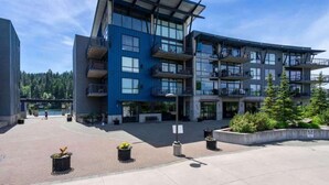 A modern multi-story building with balconies, a paved courtyard, and potted plants. - Chic Condo Steps from Spokane River And Dining (Coeur d'Alene)