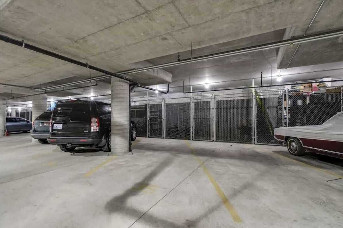 Een ondergrondse parkeergarage met betonnen pilaren, metalen hekwerk en enkele geparkeerde voertuigen.