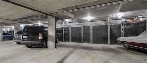 Een ondergrondse parkeergarage met betonnen pilaren, metalen hekwerk en enkele geparkeerde voertuigen.