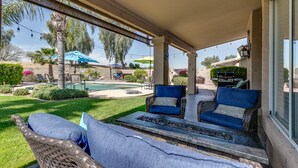 Un espacio de patio cubierto con mobiliario de mimbre, una chimenea y vistas a una piscina y jardín.