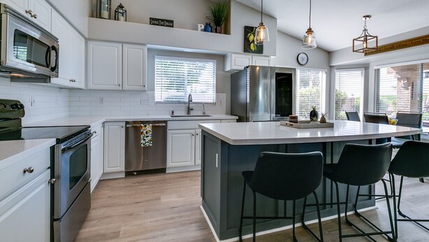 Una cocina moderna con armarios blancos, electrodomésticos de acero inoxidable, una isla central con taburetes y luces colgantes.