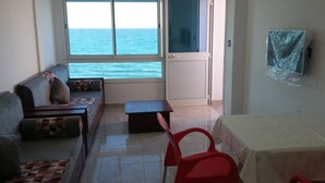 Ein Zimmer mit einer Couch, einem kleinen Tisch, einem roten Stuhl und Meerblick durch ein Fenster.