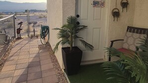 Um pátio com caminho de ladrilhos, uma porta decorada com placas de licença diversas, uma cadeira e um vaso de planta.