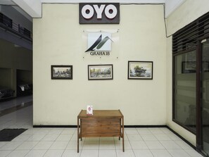 A building with a sign reading "OYO" and "GRAHA18". There are three framed pictures on the wall and a wooden table with a box on it. - Oyo 2902 Graha 18 (Surabaya)