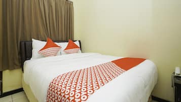 A hotel room with a bed, brown curtains, white bedding, and orange pillows.