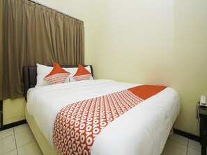 A hotel room with a bed, brown curtains, white bedding, and orange pillows. - Oyo 2902 Graha 18 (Surabaya)
