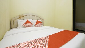 A bed with a white and orange patterned bedspread, a beige upholstered headboard, and two pillows with a red and white pattern. - Oyo 2902 Graha 18 (Surabaya)