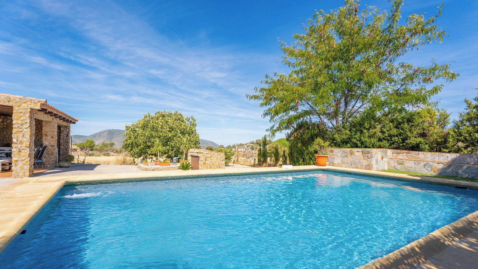 Une piscine avec des murs en pierre et un espace patio.