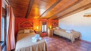 A hotel room with two beds, wooden headboards, a nightstand with a lamp, and a window with curtains.