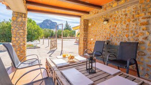 An outdoor patio with stone walls, wooden furniture, and a view of mountains.