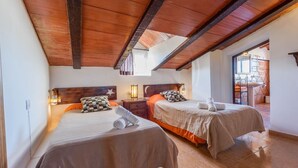 Ein Hotelzimmer mit zwei Betten, Holzbalken an der Decke, einem Nachttisch mit Lampe und Blick auf den Balkon.