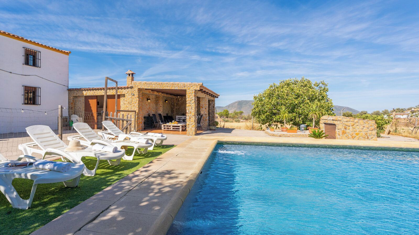 A poolside area with lounge chairs, a stone building, and a view of the landscape.