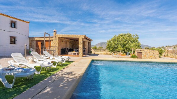 A poolside area with lounge chairs, a stone building, and a view of the landscape.